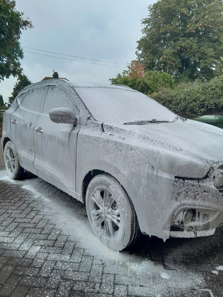 A dark hatchback covered head to toe in thick snow foam on a driveway in Hereford