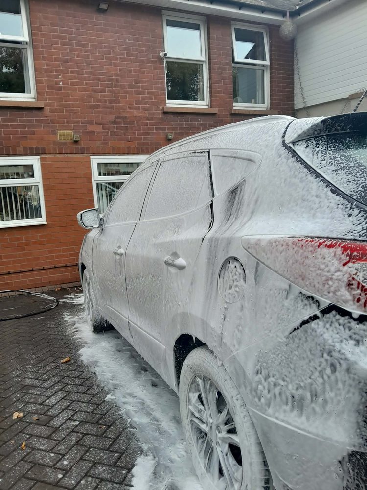 A car under a full coat of ceramic snow foam on a driveway outside a red brick house